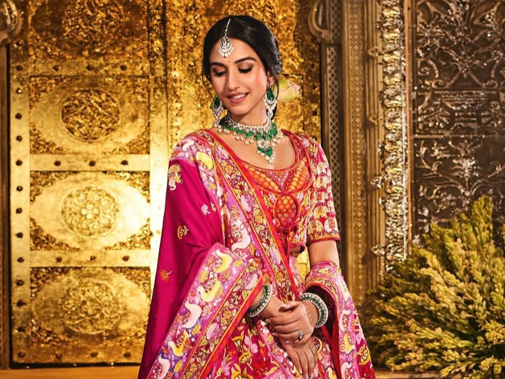 Bride in vibrant pink Rajasthani lehenga with emerald jewelry and traditional maang tikka